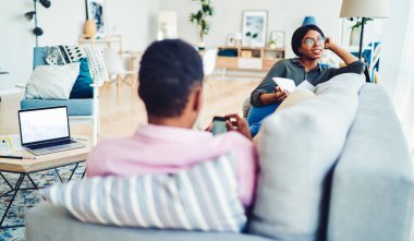 Rüya gibi Afro-Amerikan kadın gülümseyen ve bakışlarını çeviren şık oturma odasındaki kanepede kitap okurken masada boş bir dizüstü bilgisayarla