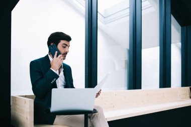 Müşteriye dizüstü bilgisayar okuma sözleşmesi imzalayan başarılı bir erkek yemliği. Çağdaş iş yerinde bankta otururken ve akıllı telefon konuşmaları yaparken.