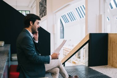 Resmi giysiler içinde çalışan Hintli erkek çalışanlar, iş arkadaşlarıyla mobil görüşmeler sırasında belgelerden bilgi okuyorlar, deneyimli yönetici iletişim kurarken raporları analiz ediyor.