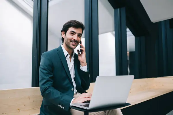 Portrait of cheerful Indian businessman smiling at camera during business conversation with corporate partner, successful South Asian male employee calling to colleague for discussing laptop data