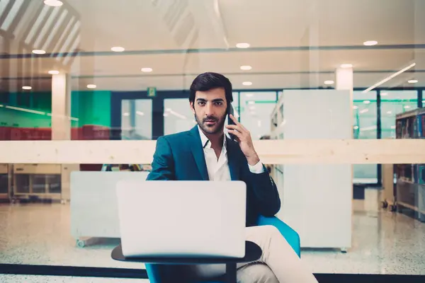 Corporate employee in formal apparel talking via mobile about status of money exchange on stock banking website, portrait of serious Indian man calling to colleague for discussing web database
