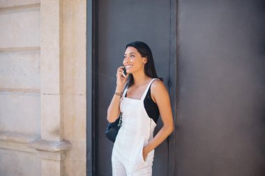 Neşeli, modaya uygun giyinmiş beyaz kadın güneşli bir günde şehir merkezinde duruyor cep telefonuyla konuşuyor, 20 'li yaşlarda hippi kız tatilde akıllı telefon görüşmesi yapıyor.