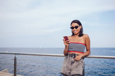 İyimser kadın turist şık kıyafetler içinde sahilde duruyor ve Roma 'da yaz tatilinde cep telefonuyla sohbet ediyor.