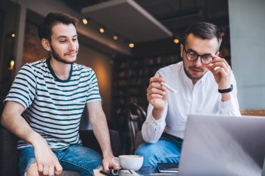 Genç adam, rahat bir kafede, masada iyimser bir meslektaşın yanında otururken bilgisayardan gelen verileri değerlendiriyor ve gözlükleri ayarlıyor.