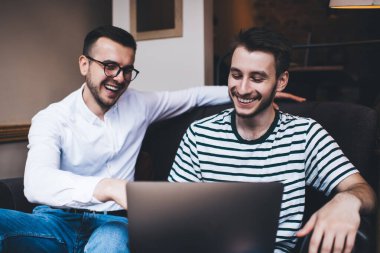 Dizlerinin üzerinde dizlerinin üzerinde oturmuş, kanepede oturmuş gülüp eğlenen zeki, şık ve neşeli genç adamlar.