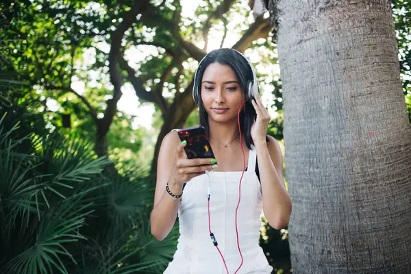 Pensive woman meloman in headphone installing app for listening playlist song on free time, beautiful female 20s millennial using smartphone installing audio book using sound accessory on leisure