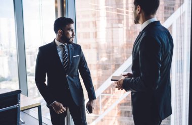 Şirket ofisindeki panoramik pencerenin yanında şık giyinmiş çeşitli meslektaşlar 30 yaşındaki çok ırklı erkek ortaklar üretken işbirliği ve beyin fırtınası brifinglerini tartışıyorlar.