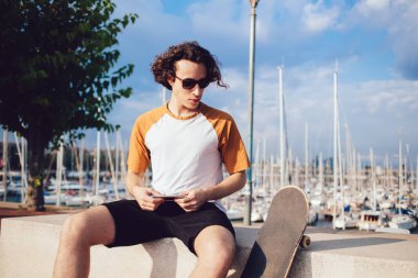 Güneş gözlüklü şık, kıvırcık saçlı adam. Güneşli bir günde Barcelona 'da kaykay yaptıktan sonra cep telefonuyla dinleniyor. 