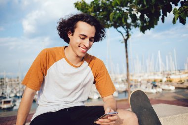 Başarılı erkek blogcu, akıllı telefon aygıtı ile çevrimiçi ağ kurma sırasında komik sosyal yayınlar okuyor, neşeli beyaz hipster adam cep telefonunda cep telefonu mesajlaşması için kablosuz ağ kullanıyor.