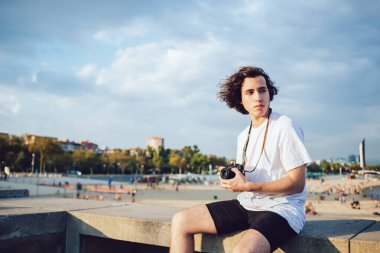 Barselona 'da şehir plajına karşı taştan çitlerde oturan sıradan bir genç adam elinde fotoğraf makinesiyle dalgın dalgın bir şekilde rüzgara bakıyor.