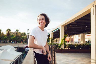 Barcelona 'da deniz kenarındaki ahşap çitlere yaslanırken ışıl ışıl gülümseyen gündelik giysiler içinde mutlu bir adamın yan görüntüsü.