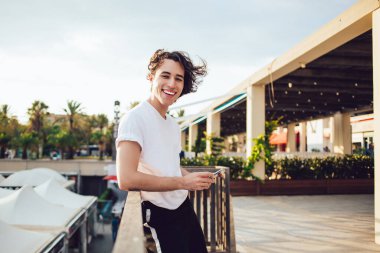 Neşeli Milenyum turisti, akıllı telefon cihazıyla seyahat sitesinde blog yazarken eğleniyor. Cep telefonunda 4G kullanan zengin bir hipsterin yarım boy portresi.