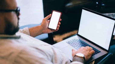 Aşırı kilolu, gözlüklü ve kol saatli uzaktan kumandalı erkek işçinin internet sayfasında yazı yazması ve iş sırasında cep telefonu kullanması yan görünüm