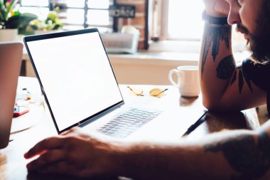 Yandan bakan sakallı erkek çalışanın dövmesi netbook boş ekranı izlerken arka tarafta rahat bir ofiste otururken...