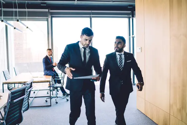 Multiracial male entrepreneurs in formal clothing communicate about business strategy analyzing paper report on way to corporate conference, businessmen discussing capital during office brainstorming