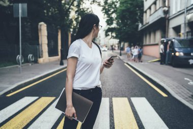 Marka etiketi için fotokopi alanı olan günlük giyinmiş bayan öğrenci kentsel caddede yaya geçidi yaparken arkasına bakıyor, çizim defteri ve akıllı telefon aygıtı için çizim defteriyle milenyum kadını