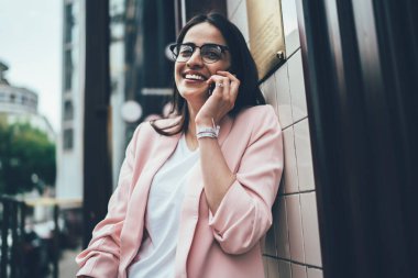 Moda gözlüklü neşeli hippi kız uluslararası iletişim numarasını çevirmek için 4G 'ye bağlanıyor ve hareketlilik uygulaması aracılığıyla arkadaşça sohbet ediyor, konuşurken mutlu kullanıcı gülüyor.