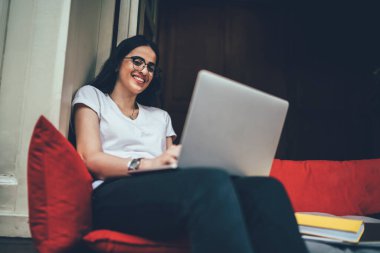 Klasik gözlüklü yetenekli bir işçinin portresi modern dizüstü bilgisayarla koltukta oturuyor ve kameraya gülümsüyor, bilgisayarlı neşeli İspanyol metin yazarı serbest yaşam tarzından keyif alıyor.