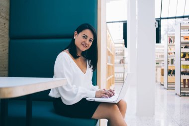 Barcelona Kafe 'de dizüstü bilgisayarla çalışırken şık giyinen, gülümseyen ve kameraya bakan çağdaş esmerin yan görüntüsü