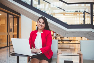 Resmi olarak genç etnik bayan çalışanlar netbook kullanıyor ve kameraya bakıp gülümserken sandalyeye oturuyorlar.