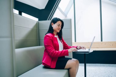 İspanyol iş kadınının resmi kıyafetleri içinde masa başında oturup bilgisayar aracılığıyla iletişim kurarken ilginç bilgiler okumasının yan görüntüsü.