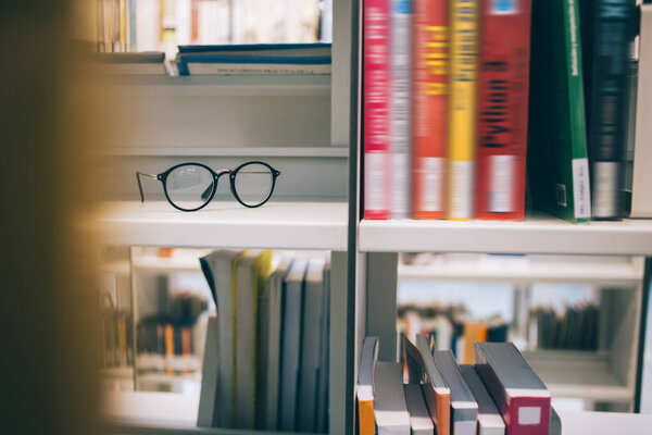 Stylish glasses with black rim placed on shelf near stacks of books in bookcase in contemporary university library in Barcelona City