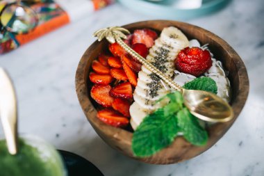 Tahta tabağın üst görüntüsü taze meyve salatası, çilek muz ve nane şekeri ve salata üzerine altın kaşık. 