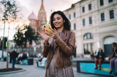 Moskova 'daki seyahatler sırasında internet üzerinden mesajlaşmak için 4G internet kullanan elektronik kulaklıklı çekici Asyalı turist, akıllı telefon ağı kurarken web yayını arayan güzel bir kadın.