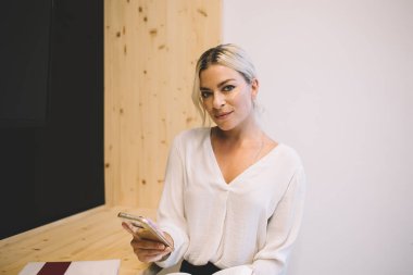 Akıllı telefondan mesajlaşırken ve modern ofisteki konferans odasında çalışırken kameraya bakan hoş bir bayan çalışan.