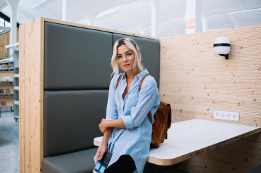 Barcelona 'da üniversite çalışma odasında elinde akıllı bir telefonla kameraya bakan ve masaya yaslanan genç ve çekici bir kız öğrenci.