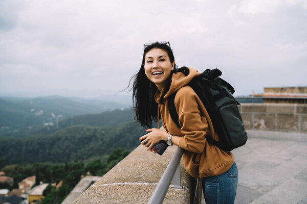 Happy asian female traveler with backpack laughing and enjoying free time on weekends explore location, smiling woman tourist excited with free time recreating on journey standing on historical place