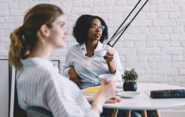 Koyu tenli, optik gözlüklü, görüş koruması için gözlüklü, elinde çay bardağıyla beyaz bir kızla yaptığı dostça görüşmede, canlı iletişim kavramını düşünmeye odaklan.