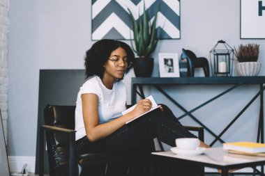 Yetenekli Afrikalı Amerikalı tasarımcı eğitim defterine çizim yapıyor. Hafta sonu evde boş zamanlarında ilginç bir proje yaratıyor. Gözlüklü çekici bir kadın, kitabında yazı yazıyor.