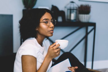 Optik gözlüklü düşünceli bir kadın romantik roman okumak için boş zamanlarında rüya görüyor, elinde kahve fincanı olan Afrikalı Amerikalı bir kadın edebiyatın en çok satan kitabını tutuyor ve düşünüyor.