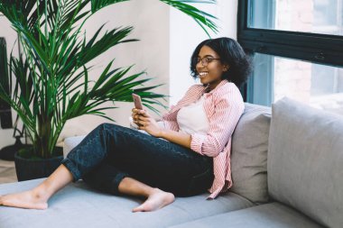 Neşeli koyu tenli blog yazarı, internet ağı kurmak için ev internetine bağlanan modern cep telefonu aygıtından e-posta alıyor, mutlu siyah kadın milenyum web sitesi rezervasyon yapmak için