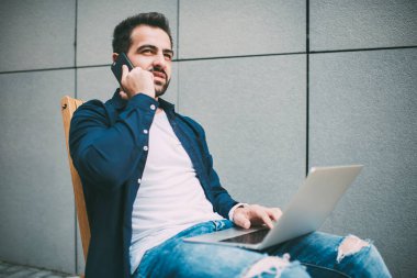 Ciddi, düşünceli, sıradan giysiler içindeki girişimci ahşap koltukta otururken ve net kitapla iletişim kurarken bulanık gri duvar karşısında gözlerini kaçırıp telefonda işini tartışıyor.