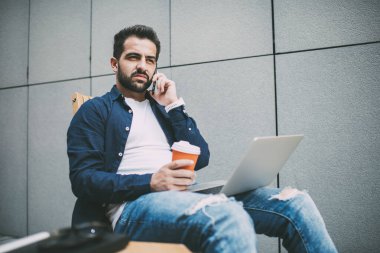 Sıcak içecekle gündelik giysiler içinde dalgın, kendine güvenen bir iş adamından sandalyeye oturmuş ve çağdaş ofiste netbook kullanırken gözlerini kaçırıp telefonla konuşmasına.