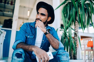 İspanyol kökenli, düşünceli, kot elbiseli ve şapkalı sakin bir erkekten. Elinde cep telefonuyla teras merdivenlerinde uzanmış başını çeviren bir şapkayla.