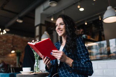 Cafe 'de oturup ilginç kitapların tadını çıkarırken şık kıyafetli, gülümseyen ve yüzünü çeviren bir kadın.