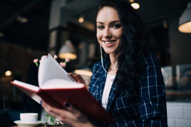 Cafe 'de müzikle kahve molası verirken şık giyinen, gülümseyen ve ilginç kitap okuyan düşük açılı bir kadın.
