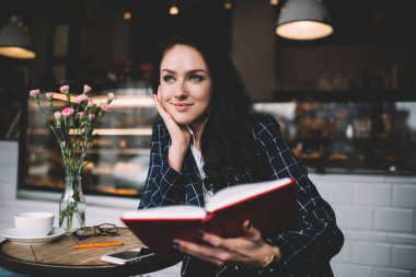 Uzun saçlı, pozitif gülümseyen bir kadın kafeteryada kitap okurken boş zamanlarında rüya gibi gözlerini kaçırıyor.