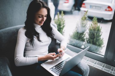 Yukardan, rahat koltukta oturan ve iş sırasında akıllı telefondan mesaj atan, rahat bir süveter giyen serbest çalışan kadın.