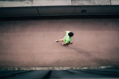 Spor giyimli, siyah saçlı, spor ayakkabılı, asfalt yolda gün ışığında beton duvar boyunca koşan bir adamdan.
