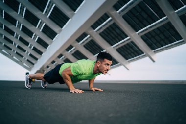 Aktif giyimli kaslı genç bir adam stadyumun beton kaldırımında antrenman yaparken yarışmaya hazırlanırken şınav çekiyor.