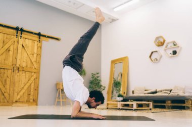 Çıplak ayaklı, zorlu Chin Stand pozu veren, spor minderinin üstünde duran ve sırt kaslarının dengesini ve esnekliğini geliştiren bir adam.