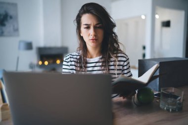 Düşünceli Kafkas hippi kız evde dizüstü bilgisayarla oturarak online kurs ödevi yapmaya odaklanmış, yetenekli genç kadın serbest çalışan postayı kontrol ediyor ve uzaktan kumandalı bir işte içeriği paylaşıyor.