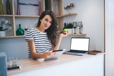 Kameraya bakan ciddi beyaz kadın portresi uzaktan kumandalı araçlar kullanarak ev içi iş yapıyor, milenyum kadını dokunmatik bilgisayarla ekranı taklit ediyor.