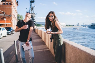 Gülen çiftin günlük kıyafetleri var. Hafta sonları boş zamanlarının keyfini çıkarıyorlar. Dalgalanan nehir ve mavi gökyüzünün arka planında toprak setin üzerinde duruyorlar.