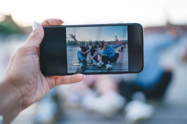 Anonim bir kadın, parkta birlikte vakit geçirirken akıllı telefondan giyinmiş bir grup arkadaşının fotoğrafını çekiyor.