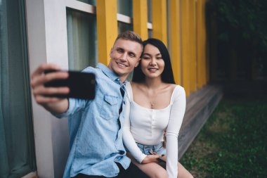 Birlikte eğlenmek için boş zamanlarında kameraya gülümseyen neşeli çift sosyal ağlara video bloğu çekiyor cep telefonlu mutlu erkek arkadaş selfie görüntüsüne tıklıyor.